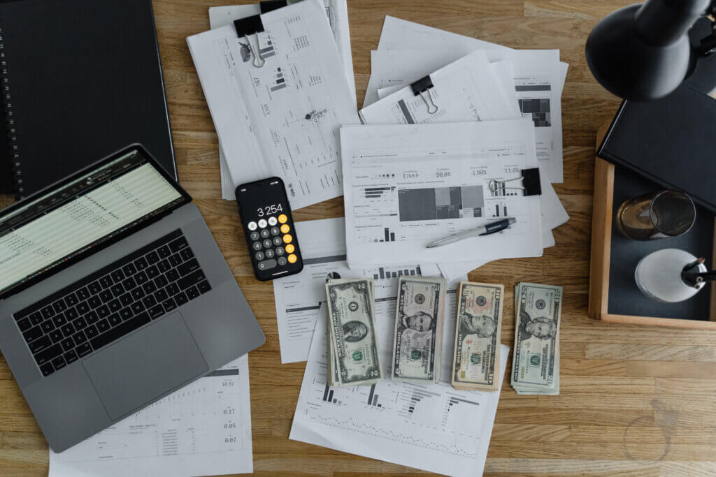 A laptop near the dollars and papers on a wooden table