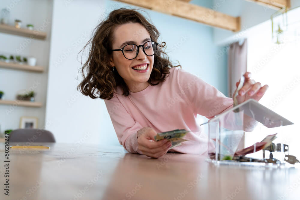 Happy woman saving money in piggy bank at home