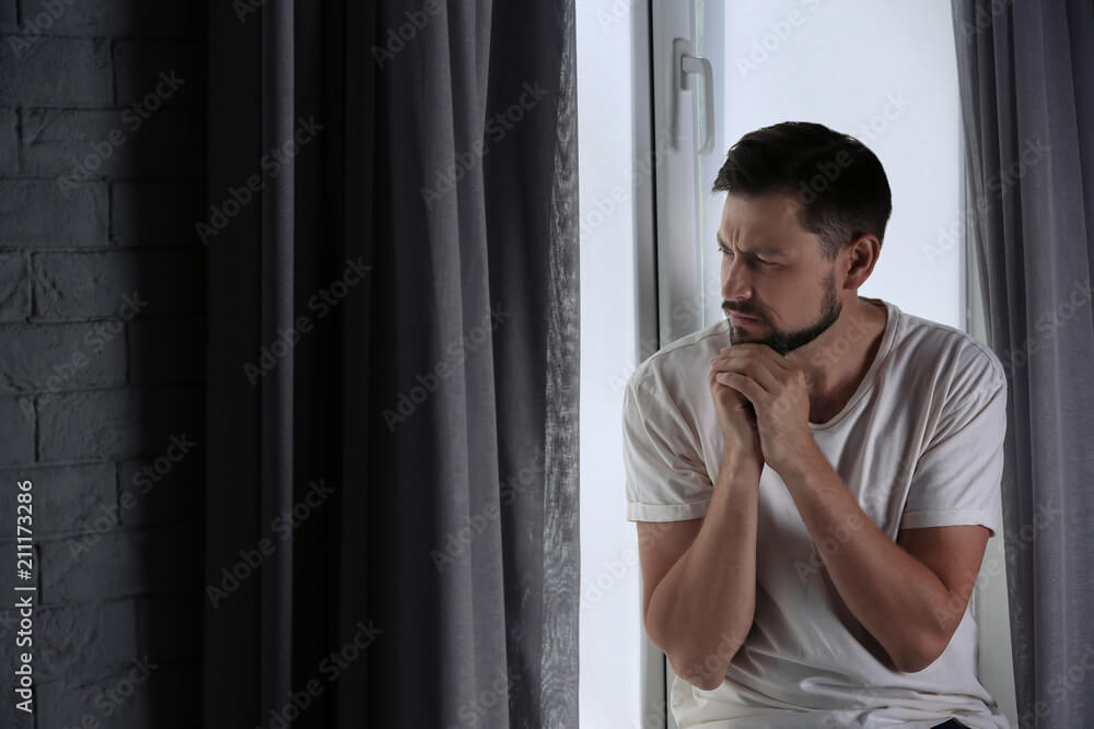 Lonely depressed man near window at home